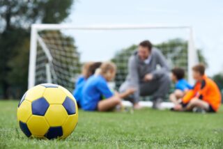 Coach,And,Team,Discussing,Soccer,Tactics,With,Ball,In,Foreground